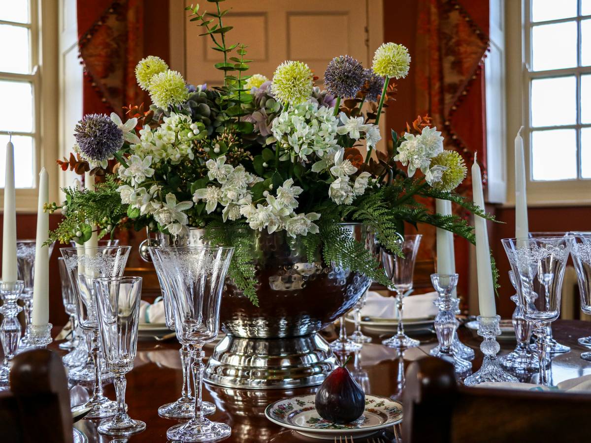 A rustic garden table centerpiece featuring weathered wood, white peonies, and hurricane lanterns on a teak outdoor table